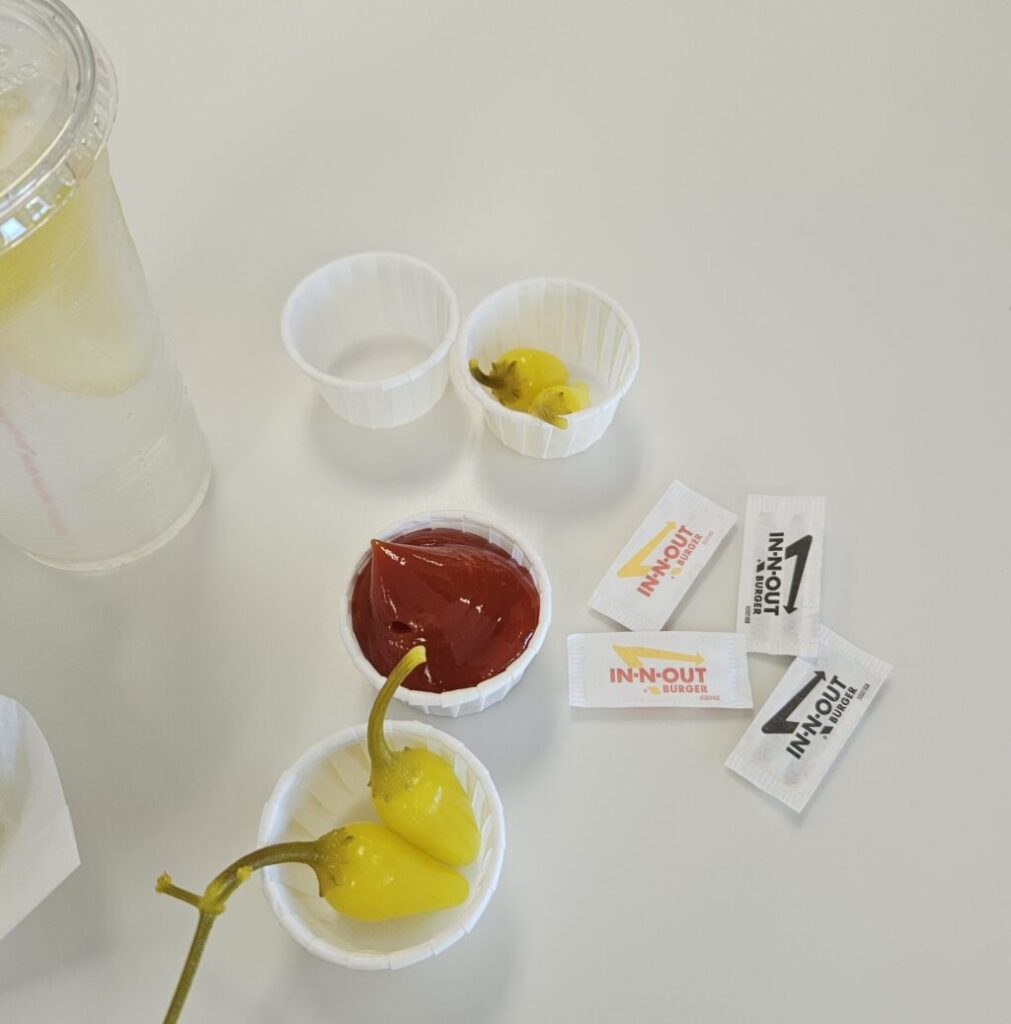 IN-N-OUTのテーブルに置かれたケチャップ、塩、ブラックペッパーの調味料と、ハラペーニョ、見切れたレモン水のグラス。